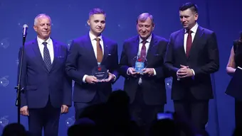 czterech mężczyzn ubranych w garnitury stoi obok siebie w rękach trzymają statuetki