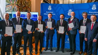 grupa mężczyzn ubranych oficjalnie stoi obok siebie w rękach trzymają dokument