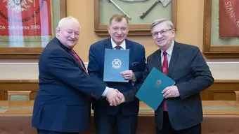 trzech mężczyzn ubranych w garnitury ściskąją sobie dłonie i trzymają w rękach teczki