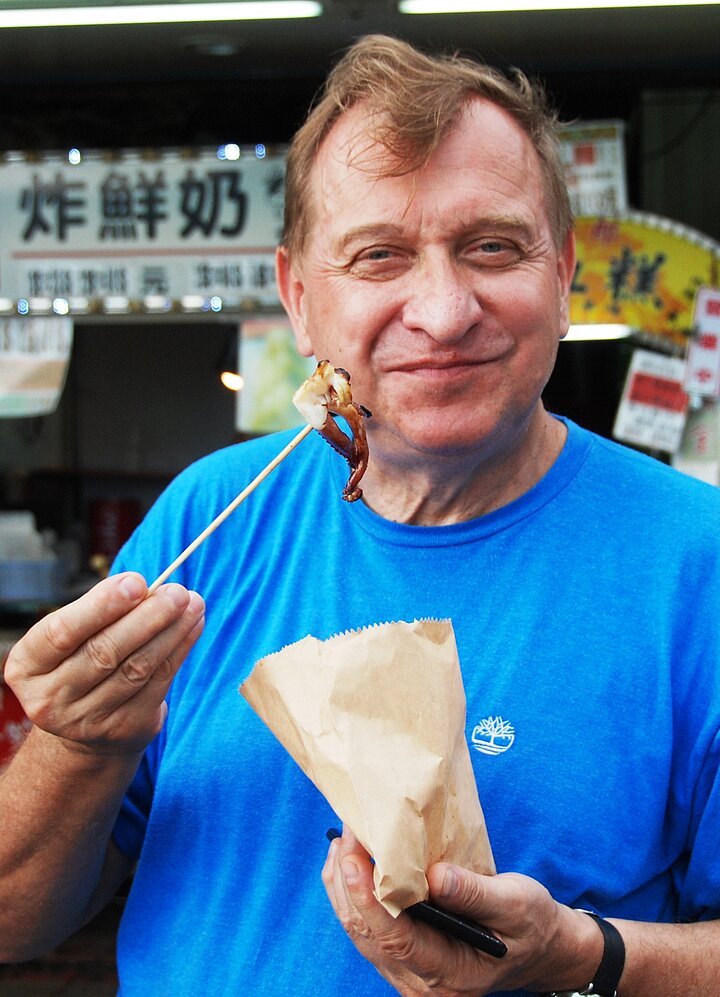 Mężczyzna ubrany casualowo trzyma w rękach patyk z nabitą ośmiornicą