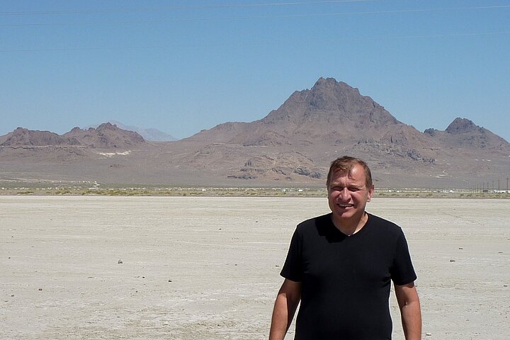 Mężczyzna ubrany w czarną koszulkę pozuje na tle gór w słoneczny dzień