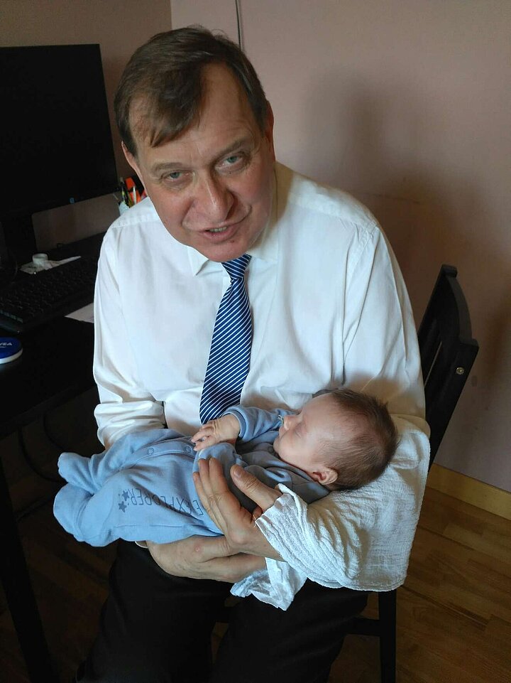 Mężczyzna ubrany w elegancką koszulę i krawat trzyma w ramionach niemowlę