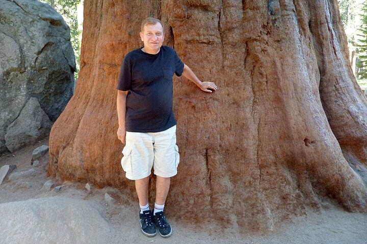 Mężczyzna ubrany casualowo pozuje na tle dużego drzewa