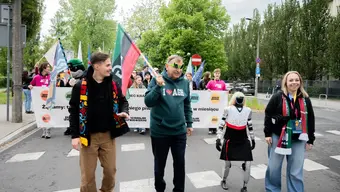 dwóch mężczyzn i kobieta oraz humanoidalny robot idą ulicą w pochodzie